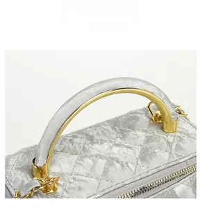 Detail of silver quilted handbag with golden arc metal handle and metallic finish