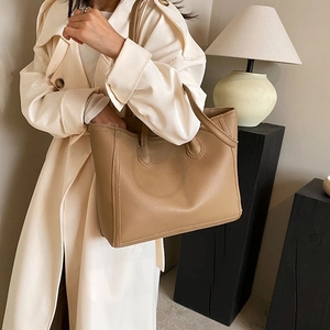 Close-up of khaki pebbled leather tote bag worn with a modern trench coat for daily commute