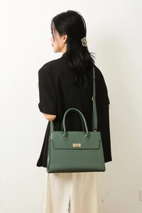 Detail of dark green tote bag with crocodile texture and gold clasp worn by a model
