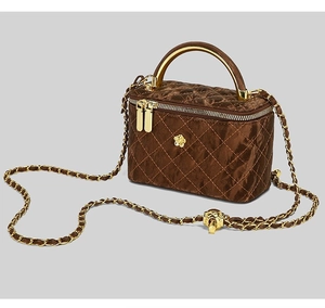 Detail of dark brown quilted velvet handbag with metal handle and floral ornament