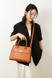 Macro detail of tan textured faux leather handbag with crocodile pattern and gold lock
