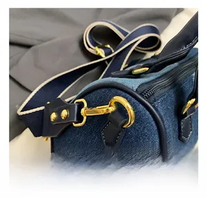 Détail du crochet en métal doré et de la sangle bleue sur le sac en jean cylindrique