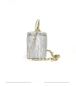 Detailed view of silver quilted cylindrical vanity bag with gold chain and handle
