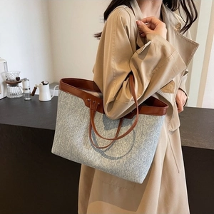 Large gray tweed tote bag with brown leather straps worn by model in trench coat