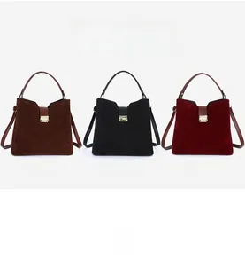 Three trapezoidal suede bucket bags in brown, black, and red with metallic clasps