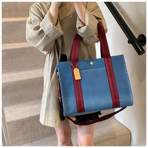 Détail d'un cabas en denim bleu foncé avec anses bordeaux et logo fleur dorée