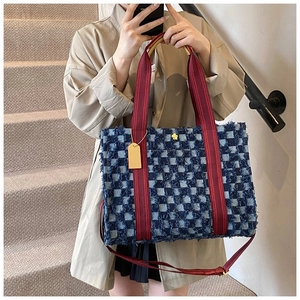Détail du sac cabas à damier bleu avec anses rouges et boucle fleur dorée