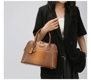 Detail of brown crocodile pattern handbag featuring a gold padlock and dual handles