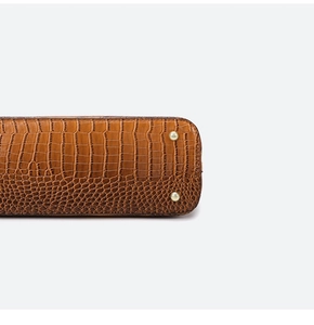 Detail of caramel brown croc-embossed leather handbag with protective gold metal feet