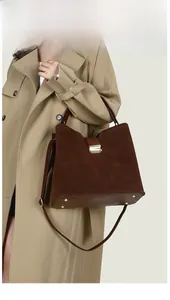 Detail of dark brown suede handbag with leather handles and gold metal clasp closure