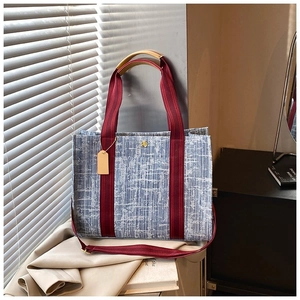Détail du sac cabas tissé bleu clair avec bandes rouges et logo métallique doré