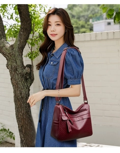 Detail of burgundy quilted faux leather crossbody bag worn with denim dress