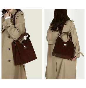 Detail view of a large vintage suede tote bag with metal buckle on a beige trench coat