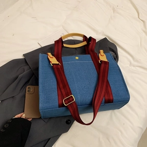 Détail du sac cabas en denim bleu avec anses rayées rouge et marron et bouton fleur