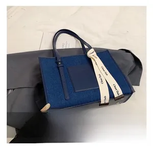 Detailed view of denim tote bag with leather pocket, logo ribbon, and metal rivets