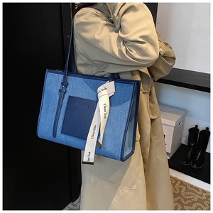 Detail of blue denim tote bag featuring leather pocket and woven logo strap styling