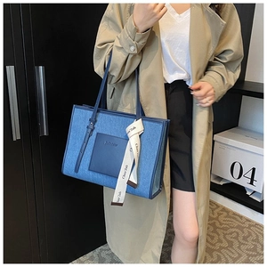 Detail view of denim and leather tote bag with elegant silk scarf on shoulder strap