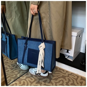 Detail of denim tote bag featuring navy leather handles and decorative printed silk ribbon