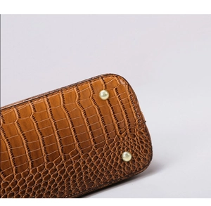 Detail view of brown crocodile texture handbag base with protective metal studs