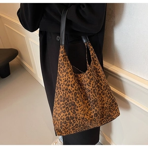 Model wearing a large leopard print tote bag with black shoulder straps in a minimalist setting