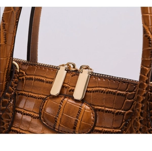 Detail view of double gold zippers and crocodile embossed texture on a brown handbag