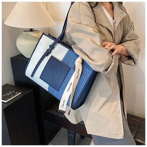 Detail of canvas tote bag featuring denim patchwork and white lettered webbing strap