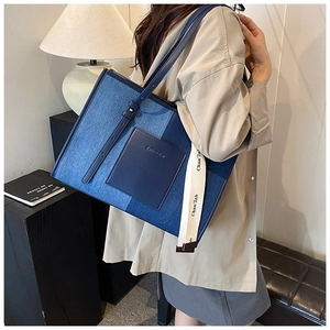 Detail of high-capacity denim patchwork tote bag with stylish wide logo strap and leather pocket