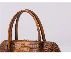 Close-up of brown crocodile embossed leather handbag featuring dual zippers and top handles