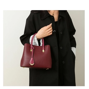 Detail of burgundy pebbled leather handbag with gold hardware and crocodile texture tag