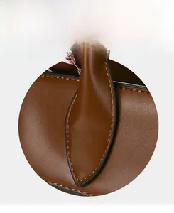 Detail of leaf-shaped handle reinforcement on brown leather tote with precise stitching