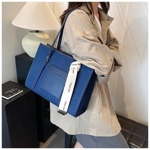 Detail of blue canvas tote bag featuring branded lettered straps and leather patch
