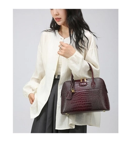 Detail of burgundy crocodile pattern leather handbag with gold hardware and top handles