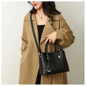 Detail of black lychee grain tote bag with gold hardware and shield charm on khaki coat