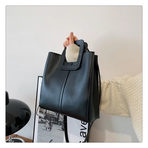 Detail of black matte leather tote bag featuring unique square cutout handle and stitching