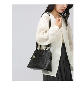 Close-up of black crocodile texture handbag with gold padlock and metal protective feet