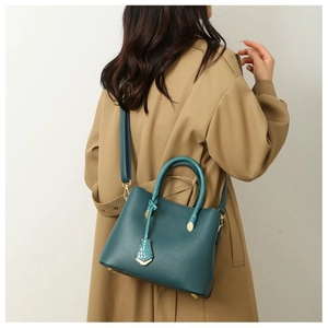 Detail of dark teal crossbody bag with snake pattern charm on khaki trench coat