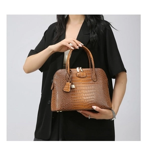 Detail of dark brown crocodile texture handbag with metal padlock and polished leather