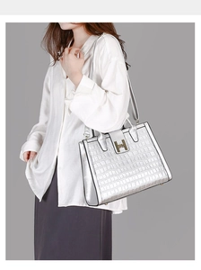 Close-up of silver tote bag with crocodile texture and golden H-shaped metal buckle
