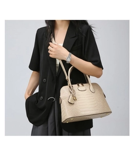 Detail of beige crocodile pattern shell handbag with gold hardware and shoulder strap