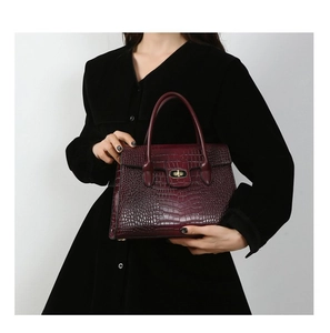 Detail of burgundy tote bag with crocodile embossed texture and metal clasp closure
