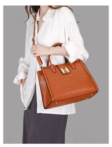 Macro view of brown crocodile texture leather and golden H-shaped clasp on tote bag
