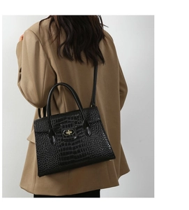 Detail view of black crocodile pattern handbag with golden twist lock and top handles
