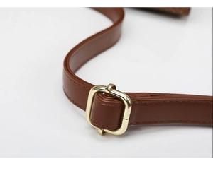 Detail of a brown leather strap featuring a golden metal buckle and fine stitching