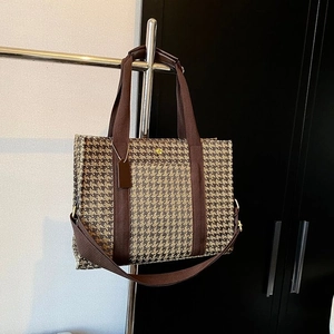 Detail of houndstooth tote bag featuring brown straps and golden circular logo