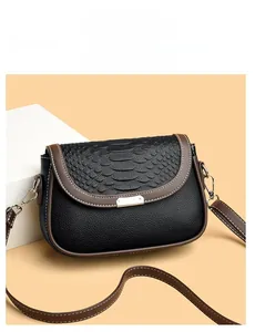 Détail de la texture grainée noire avec bordure marron et boucle en métal sur le sac bandoulière
