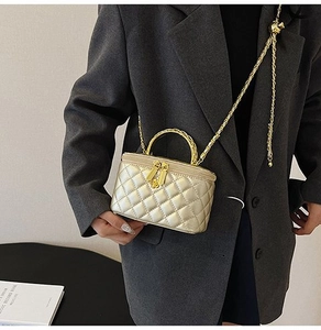 Detail of champagne gold quilted box bag with metal handle and chain strap on shoulder