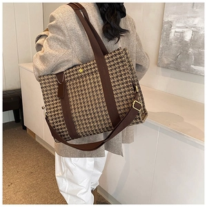 Model wearing a large houndstooth tote bag with brown canvas straps in a modern room