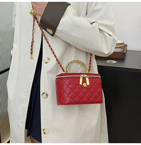 Detail of red quilted crossbody bag with gold chain strap and metal top handle