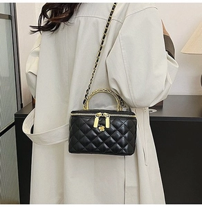 Detail of black quilted vanity bag with gold chain strap and floral zipper charm
