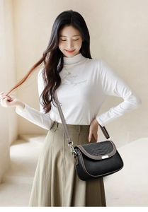 Détail du sac bandoulière en cuir noir avec bordure marron et boucle argentée